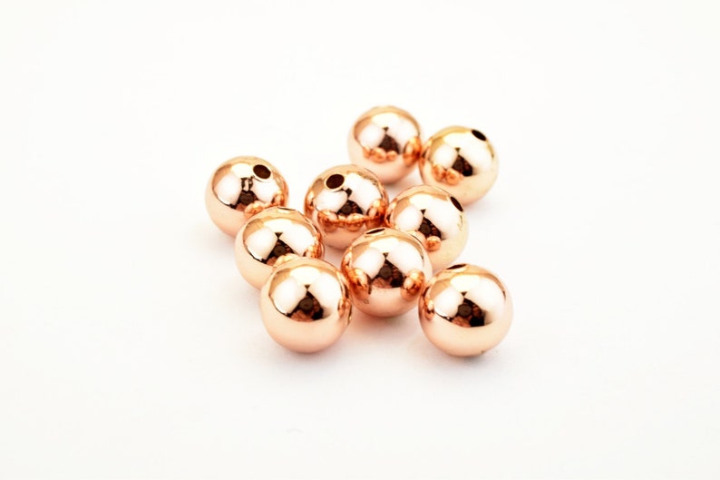 Peut inclure: Un groupe de dix perles en m&eacute;tal de couleur or rose. Les perles sont rondes et ont une finition lisse et brillante.