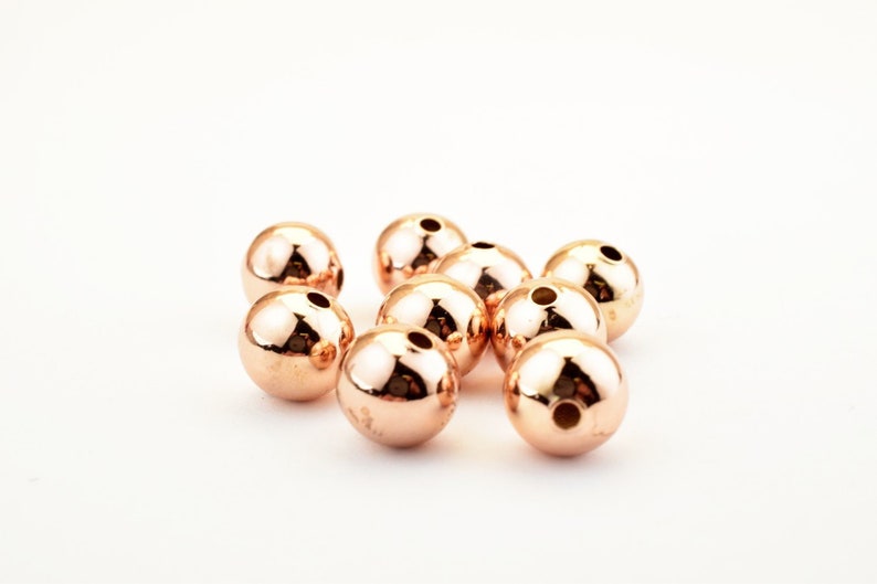 Peut inclure: Un groupe de dix perles rondes en or rose. Les perles sont lisses et brillantes.