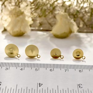 May include: Four gold-colored earring backs of different sizes, measured in inches on a ruler. The backs have a small loop on the side.