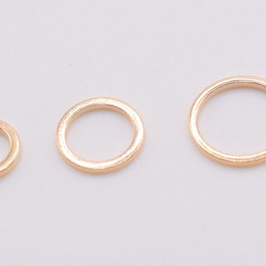 May include: Three circular metal rings in a rose gold tone, arranged in a horizontal row from smallest to largest. Each ring features a smooth, polished surface and a simple, continuous band design, showcasing a consistent metallic finish.