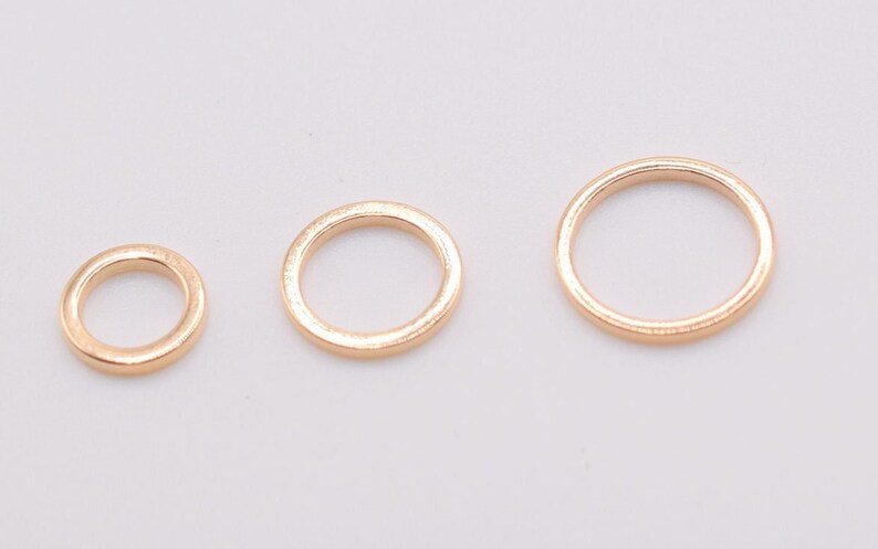 May include: Three circular metal rings in a rose gold tone, arranged in a horizontal row from smallest to largest. Each ring features a smooth, polished surface and a simple, continuous band design, showcasing a consistent metallic finish.