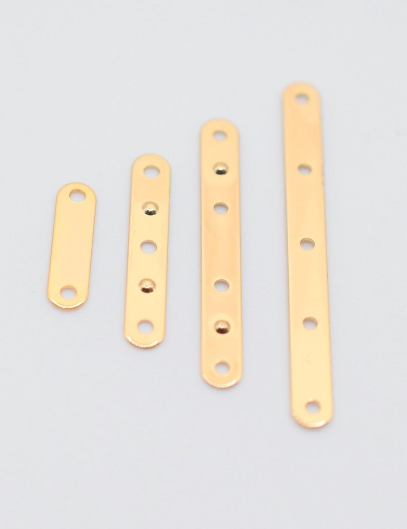 May include: Four gold-colored metal connector bars of varying lengths, each with evenly spaced holes for attaching components. The bars are arranged vertically against a light gray background, showcasing their polished finish and design.