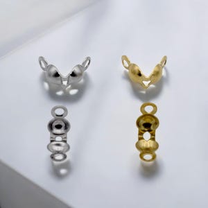 May include: Close-up of jewelry findings in silver and gold tones. The findings include V-shaped components with loops and elongated pieces with multiple rounded sections and loops, all against a white background.