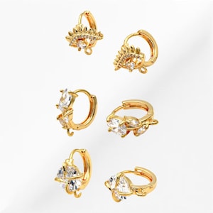 May include: Set of six gold hoop earrings with clear crystal accents. The earrings feature different designs, including a teardrop shape, a geometric shape, and a leaf shape.