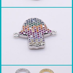 May include: Three different charm pendants for jewelry making. The first is a gold-toned seashell charm with clear rhinestones. The second is a silver-toned hamsa hand charm with multi-colored rhinestones. The third is a silver-toned and gold-toned evil eye charm with blue rhinestones.