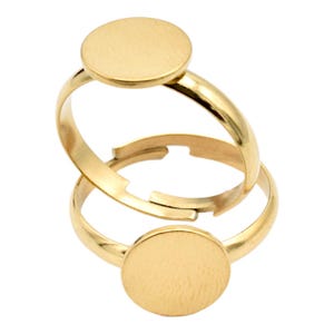May include: Two gold-toned adjustable rings with round, flat, blank metal tops. The rings are designed for adding charms or other embellishments.