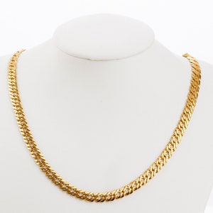 Puede incluir: Un collar de cadena de oro con un dise&ntilde;o de eslabones curb. La cadena se muestra en un maniqu&iacute; blanco.