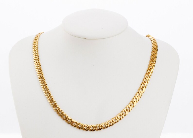 Puede incluir: Un collar de cadena de oro con un dise&ntilde;o de eslabones curb. La cadena se muestra en un maniqu&iacute; blanco.