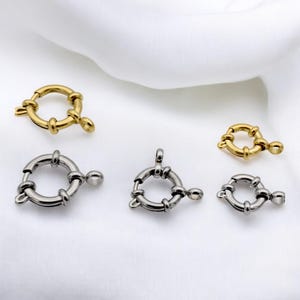 May include: A collection of four circular spring ring clasps for jewelry making. Two clasps are finished in a polished gold tone, and two are finished in a polished silver tone. Each clasp features a small spring-loaded mechanism and a loop.