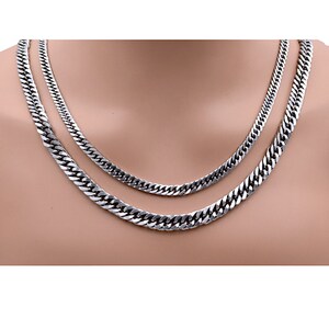 Puede incluir: Dos collares de cadena de eslabones plateados de diferentes longitudes. Los collares se muestran sobre un fondo neutro. Las cadenas tienen un aspecto brillante y metálico y un diseño clásico.