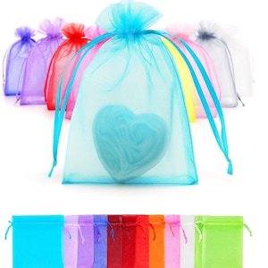 May include: A collection of colorful organza gift bags. A light blue bag in the foreground contains a blue heart-shaped object. Other bags are in shades of purple, red, pink, yellow, and green. Each bag has a drawstring closure.
