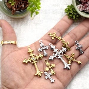 May include: A collection of ornate cross charms in gold, silver, and brass tones. Some crosses feature a central gemstone. The charms vary in size and design, with intricate details and loops for attaching to jewelry.