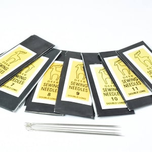 May include: A set of ten black sewing needle packages with a yellow deer logo and the text "Deer Sewing Needles" and the size of the needle. The needles are double long.
