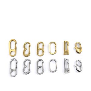 May include: An assortment of metal clasps in gold and silver tones. The clasps vary in shape, including oval, rectangular, and curved designs. The clasps are arranged on a white background, showcasing their different styles and finishes.