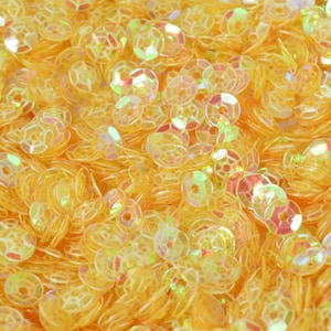 Può includere: Primo piano di un mucchio di paillettes gialle iridescenti. Le paillettes sono rotonde e hanno un design sfaccettato.