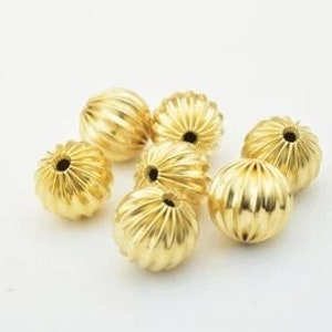 May include: Six gold-colored round beads with a ribbed texture. The beads have a hole in the center for stringing.