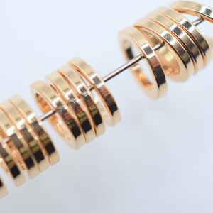 May include: A series of small, polished gold-toned metal rings with a flat, circular profile, threaded onto a thin, straight metal wire. The rings feature a smooth, reflective surface and are arranged in two distinct groups along the wire.