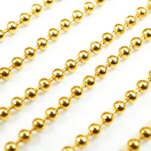 May include: A close-up of four strands of gold ball chain. The chain is made of small, round, shiny gold beads.