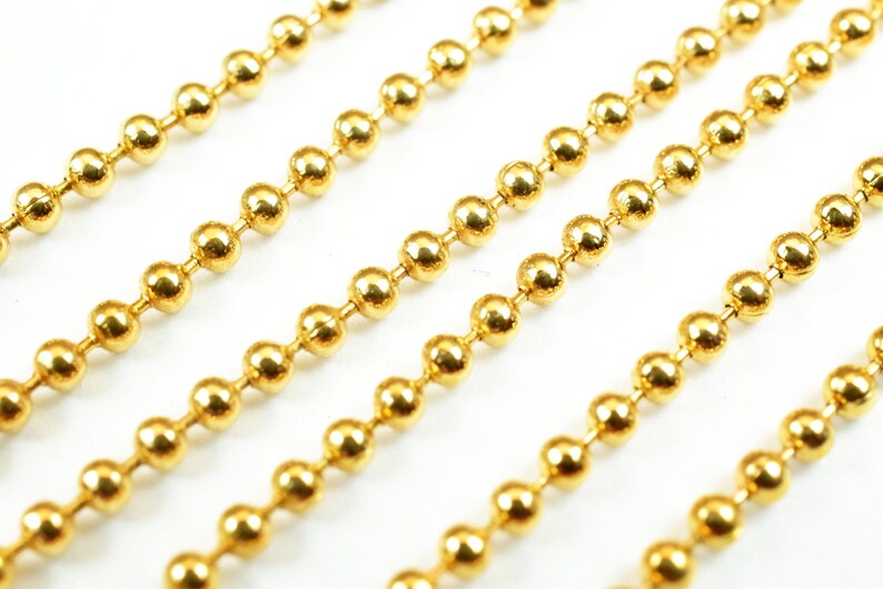 May include: A close-up of four strands of gold ball chain. The chain is made of small, round, shiny gold beads.