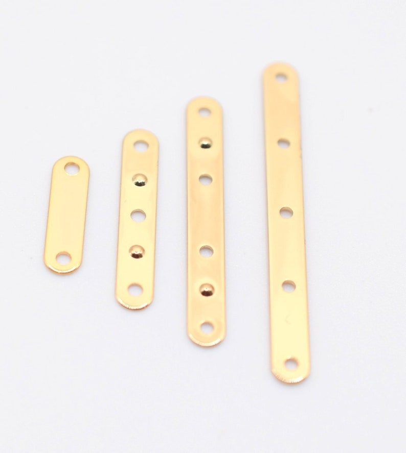 May include: Four gold-colored metal connector bars of varying lengths, each with evenly spaced holes for screws or fasteners. The bars are arranged vertically against a white background, showcasing their polished, reflective surface. These are likely used in jewelry making or small craft projects.