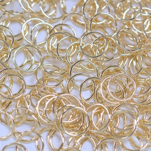 May include: A large pile of gold jump rings. The rings are all the same size and are arranged in a random pattern.