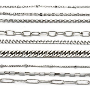 May include: A collection of silver-colored chain necklaces in various styles. The chains include delicate beaded, oval link, curb, and box chain designs. The necklaces are displayed against a white background, showcasing their different textures and patterns.