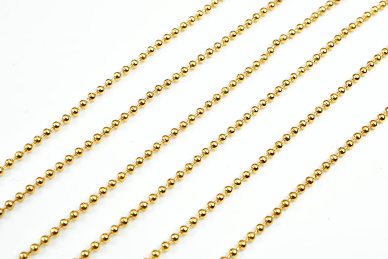 May include: Gold ball chain, a type of jewelry chain made of small, round beads connected together. The chain is shown in a straight line, with multiple strands laid out parallel to each other.