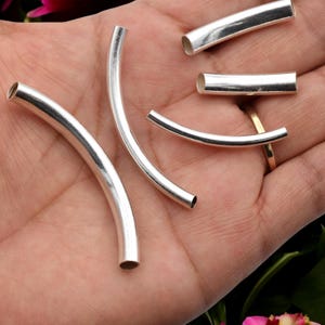 May include: Several silver-colored, curved metal tubes of varying lengths. The tubes have a polished finish and are open at both ends. The tubes are arranged on a light-colored surface, with some tubes curved and others straight.