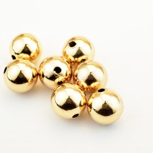 May include: Seven shiny, gold-colored, spherical beads with small holes. The beads are smooth and reflective, catching the light. These beads are likely for jewelry making or other craft projects.