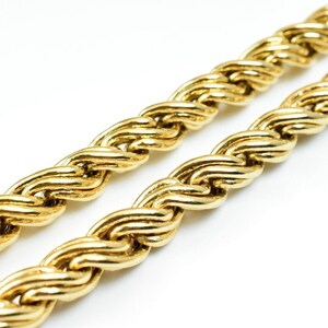 May include: A close-up of a gold rope chain necklace. The chain is made of thick, interwoven links, creating a textured and luxurious look.