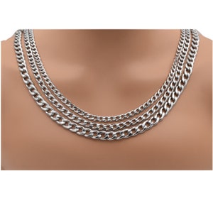 May include: Three silver-colored curb chain necklaces of varying thicknesses are displayed. The necklaces are arranged to cascade down, showcasing the different chain sizes. The chains have a polished, reflective surface.