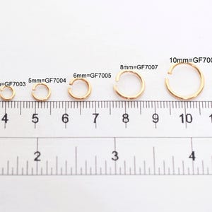 May include: A series of eight gold-colored metal jump rings arranged by size above a ruler. The rings are labeled with their diameters and product codes: 2mm=GF7001, 3mm=GF7002, 4mm=GF7003, 5mm=GF7004, 6mm=GF7005, 8mm=GF7007, 10mm=GF7009, and 12mm=GF7010.