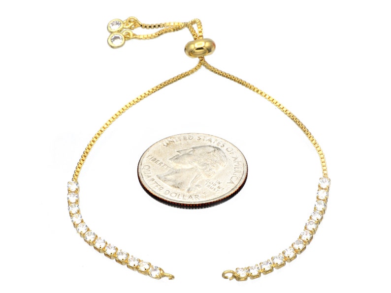Puede incluir: Un brazalete de cadena dorada con un cierre deslizante y una fila de piedras de circonita c&uacute;bica transparentes. El brazalete se muestra junto a una moneda de 1 euro para referencia de tama&ntilde;o.