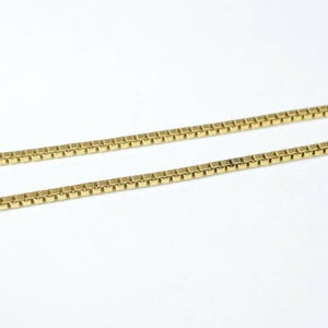 A close-up image of a gold-colored necklace chain with square links.