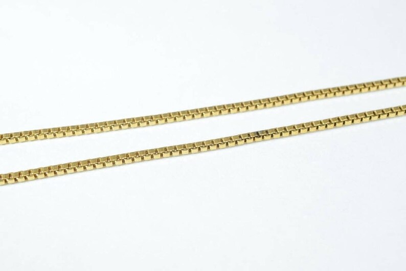 A close-up image of a gold-colored necklace chain with square links.