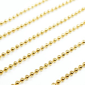 May include: Four strands of gold ball chain, a type of jewelry chain, are laid out in parallel lines on a white background.