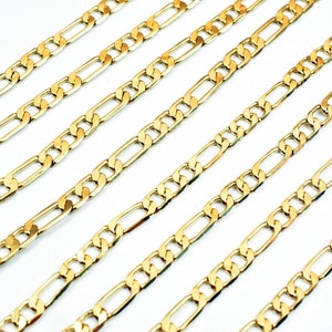 May include: Multiple gold-coloured chains with a figaro link pattern. The chains are laid out in parallel lines on a white background.