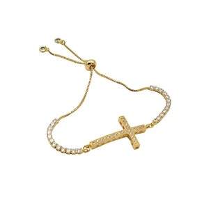 Puede incluir: Un brazalete ajustable de oro con un dije de cruz. La cruz est&aacute; incrustada con piedras de circonita c&uacute;bica transparentes.