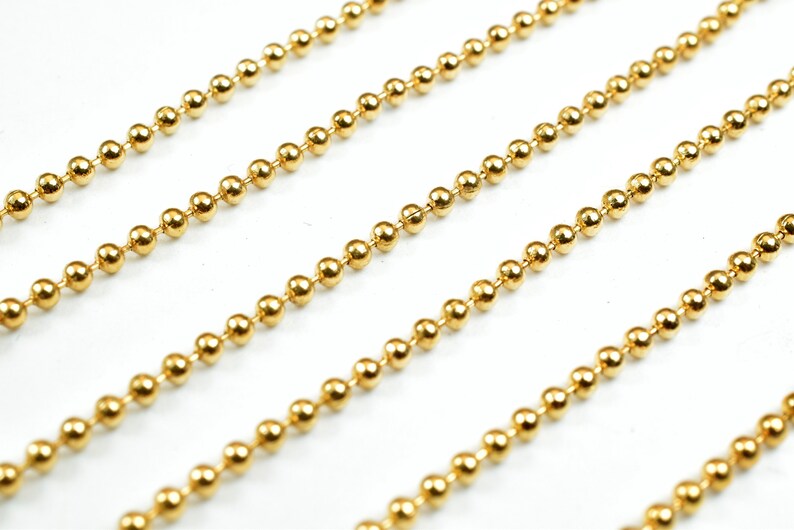 May include: A close-up of a gold ball chain. The chain is made of small, round beads that are linked together.
