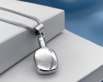 May include: A silver chain necklace with a silver pendant shaped like a small bottle. The pendant has a smooth, shiny surface.