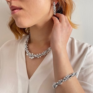Puede incluir: Un collar y una pulsera de plata con un diseño de cuentas. El collar se lleva alrededor del cuello y la pulsera se lleva en la muñeca.