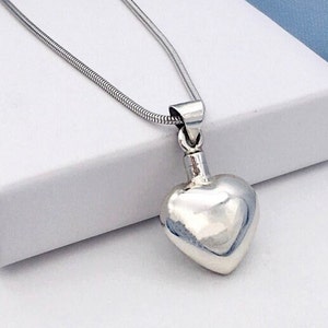 Puede incluir: Un collar de plata con un colgante en forma de coraz&oacute;n y una cadena delicada. El colgante es liso y brillante, y la cadena es una cadena de serpiente.