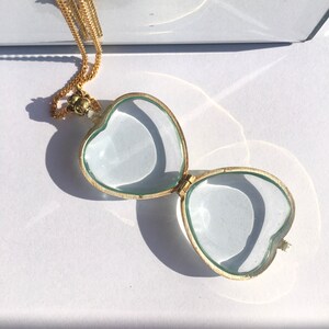 May include: A gold heart-shaped locket necklace with a clear glass lid. The locket is open, revealing the empty interior.