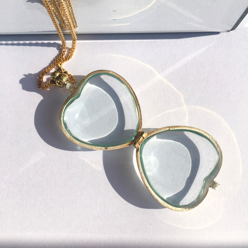 May include: A gold heart-shaped locket necklace with a clear glass lid. The locket is open, revealing the empty interior.