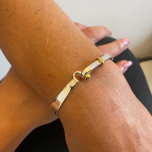 May include: A silver and gold bangle bracelet with a hinged clasp. The bracelet is made of two different metals, with a silver band and a gold clasp.
