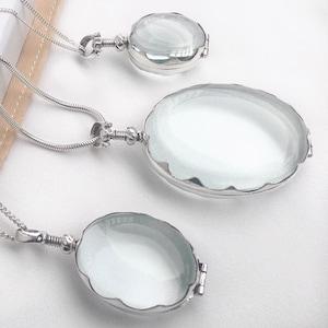 Op de afbeelding: Drie zilveren kettingen met hangers in de vorm van ovale, transparante glazen medaillons. De medaillons zijn van verschillende grootte en hangen voor een witte achtergrond.