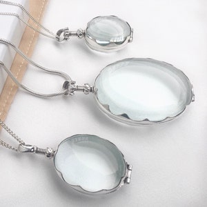 May include: Three silver locket necklaces with oval-shaped glass pendants. The lockets are different sizes and hang from delicate silver chains.