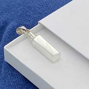 May include: A silver pendant in the shape of a small rectangular bottle. The pendant is in a white box.