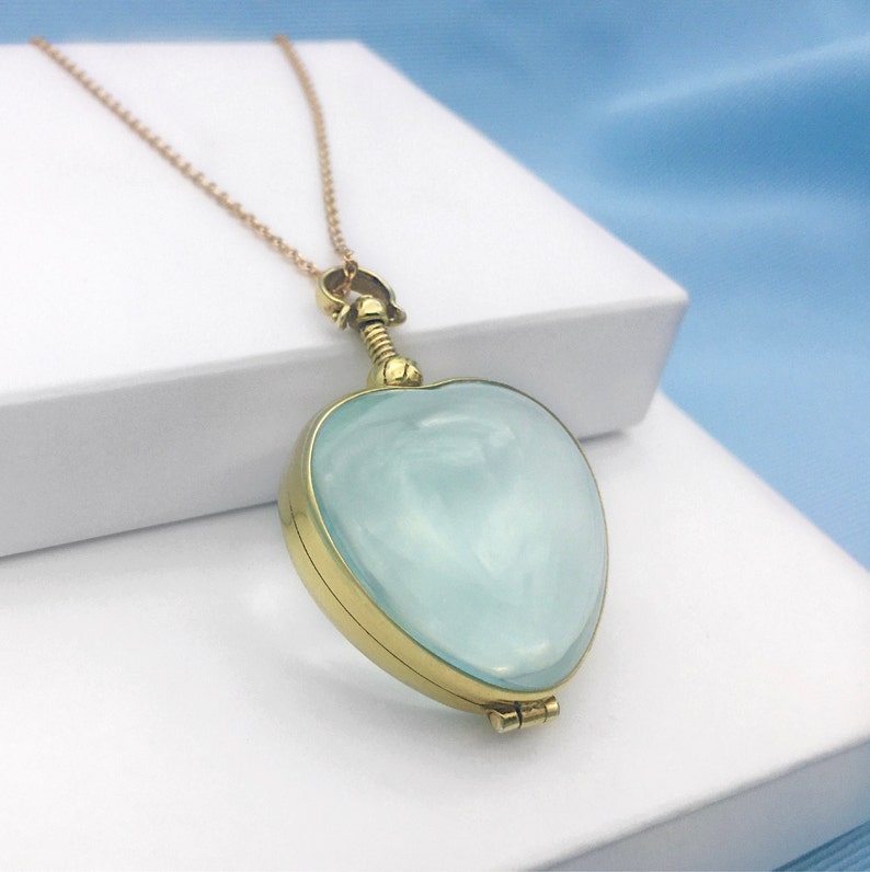 May include: A gold heart-shaped locket necklace with a light blue glass insert. The locket is open and the chain is visible.