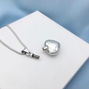Puede incluir: Un collar de plata con un colgante en forma de coraz&oacute;n y una cadena. El colgante es una peque&ntilde;a botella con una tapa de rosca.